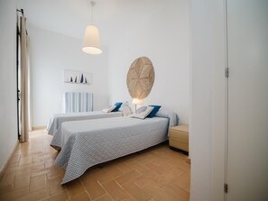A bedroom with two beds, a large woven wall hanging, and a hanging light fixture.