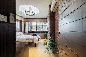 Une chambre d’hôtel compacte comprenant un lit, une table de chevet, une plante en pot et une vue sur la ville grâce à de grandes fenêtres.