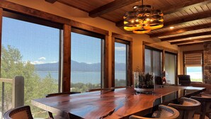 A large wooden dining table with chairs, large windows with a view of a lake and mountains, and a modern pendant light. - NEW in 2026! Elegant, Dramatic Mountain/Lake Views! 20 Mins to Yellowstone NP! (Island Park)