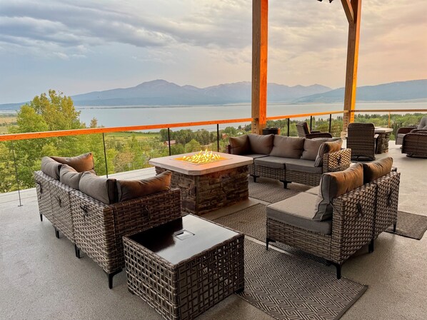 Une terrasse dotée de meubles en osier, d’une table en pierre et offrant une vue sur les montagnes et un lac.