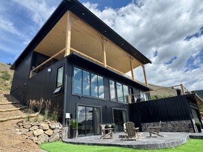 Une maison moderne à deux étages, dotée de grandes fenêtres, d’un patio couvert et d’un mur de soutènement en pierre.