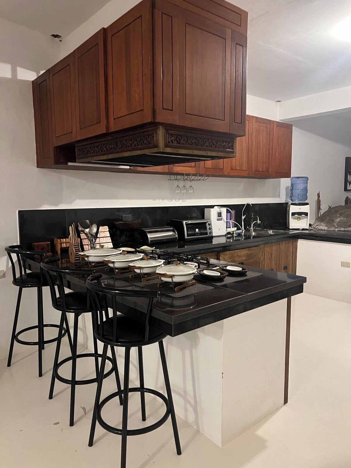 A kitchen with wooden cabinets, a black countertop, a gas stove, a toaster, and bar stools.