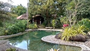 Een rustige tuin met een rond zwembad, weelderige begroeiing en een eenvoudige hut.
