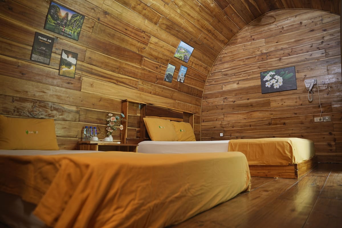 A wooden cabin-style room with two beds, a wooden ceiling, and framed pictures on the walls.