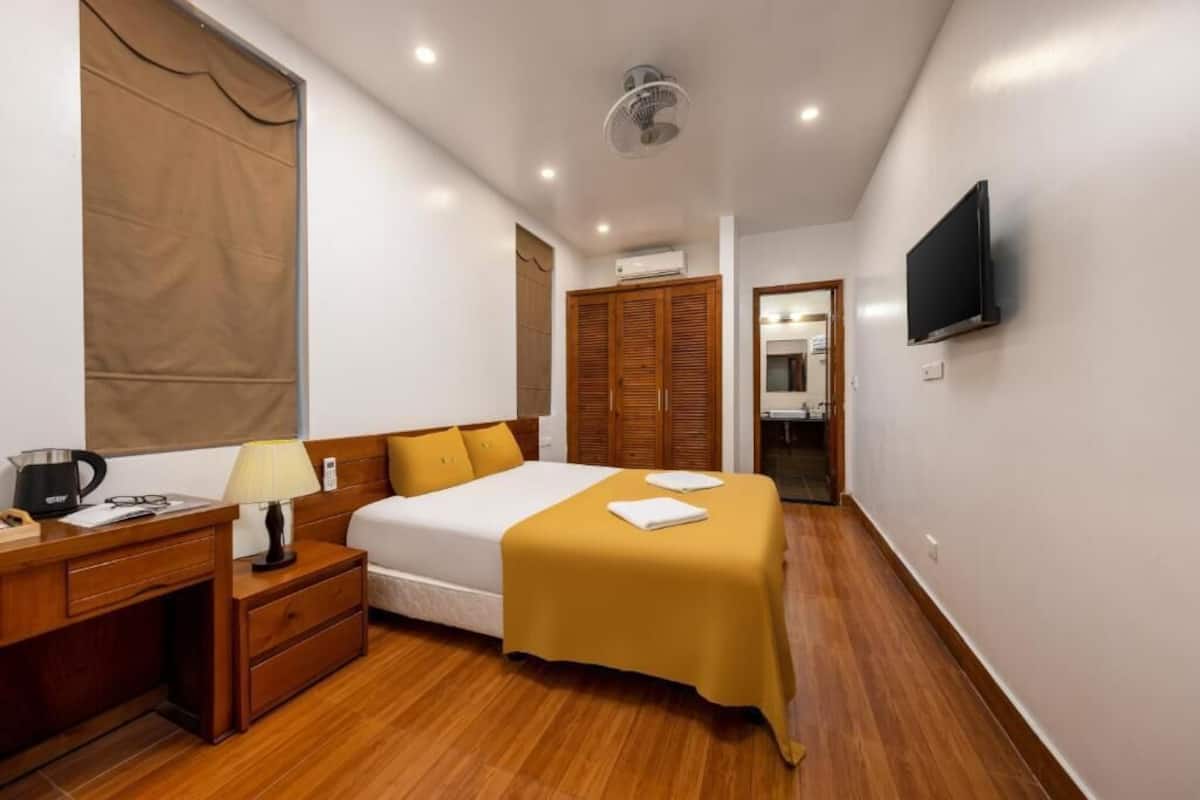 A hotel room with a bed, bedside table, lamp, and a TV mounted on the wall.
