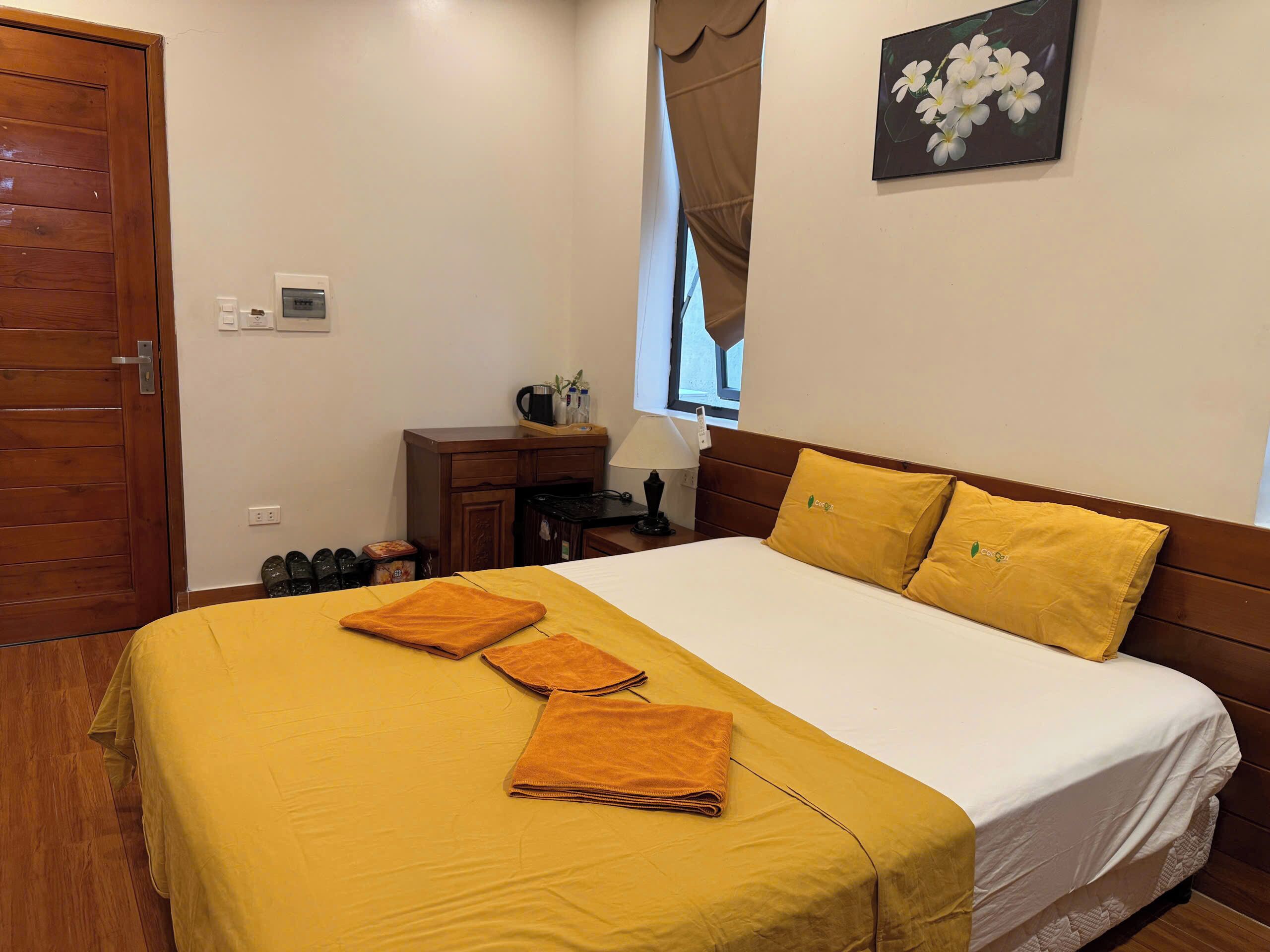A hotel room with a bed, a desk, a chair, a lamp, a window with curtains, and a picture on the wall.