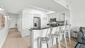 A modern kitchen with white cabinetry, a central island with bar stools, and a microwave above the island. - Ariel Dunes II in Seascape Resort! 405 (Miramar Beach)