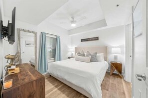 A bedroom with a bed, bedside tables, a TV, and a ceiling fan.