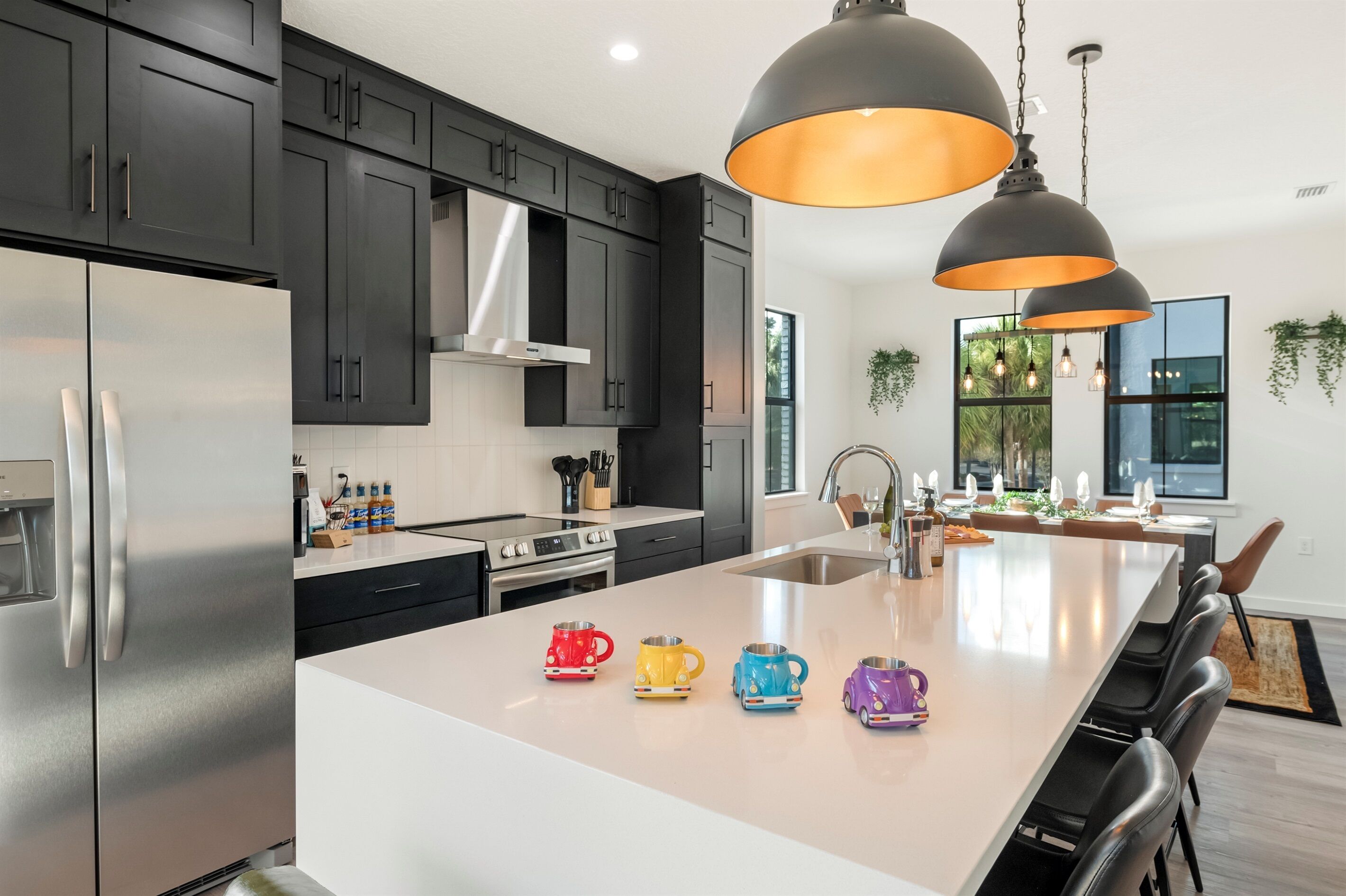 A modern kitchen with dark cabinets, stainless steel appliances, and a central island with colorful mugs.