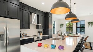 A modern kitchen with dark cabinets, stainless steel appliances, and a central island with colorful mugs.