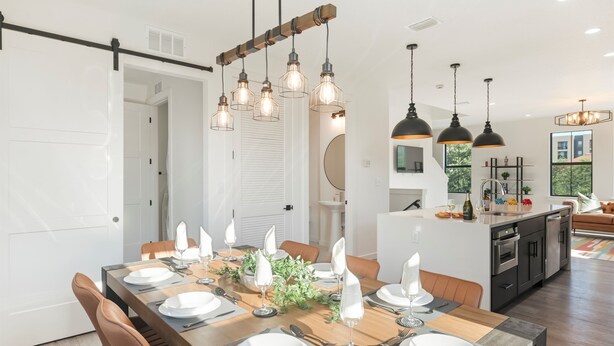 A modern dining area with a wooden table set for six, surrounded by brown leather chairs.