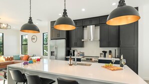 A modern kitchen with dark cabinets, a large island with bar stools, and pendant lighting.