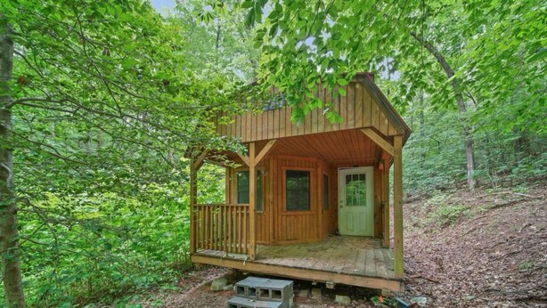 A wooden cabin with a porch, set in a forested area.
