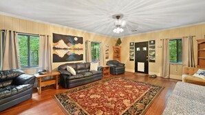 A spacious living room with a large painting, leather sofas, a red patterned rug, and wooden flooring.