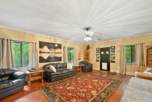 A spacious living room with a large painting, leather sofas, a red patterned rug, and wooden flooring.