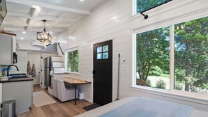 Une cuisine moderne avec des meubles blancs, un plan de travail en bois et une porte noire. Une grande fenêtre offre une vue sur les arbres.