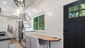Une cuisine moderne avec un lambris blanc, un banc intégré, une porte noire et une fenêtre donnant sur la forêt.