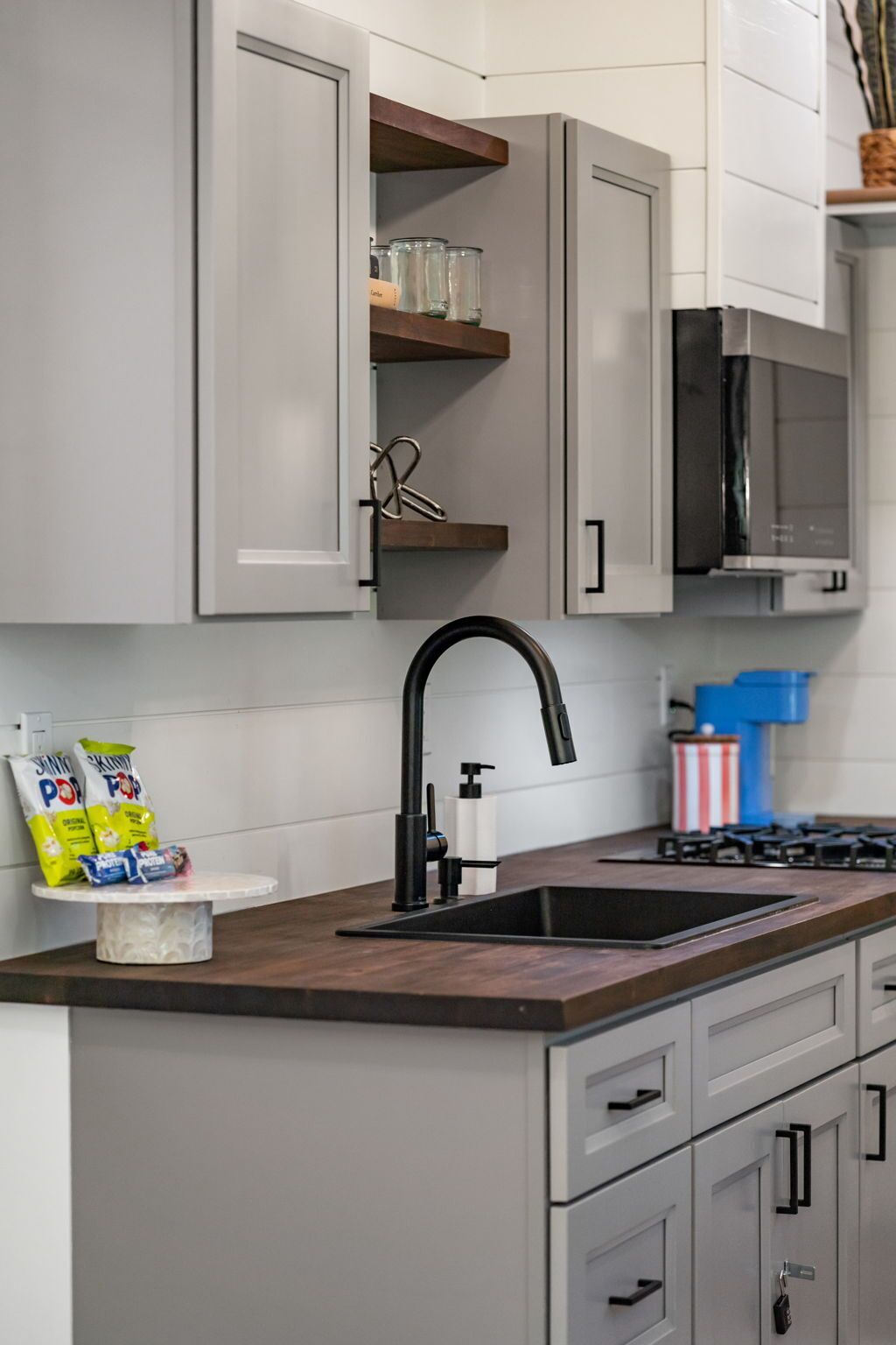 A kitchen with grey cabinets, a black faucet, and a microwave.