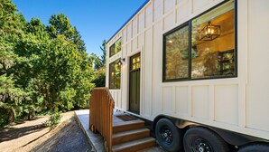 Une maison mobile dotée d’un escalier en bois menant à l’entrée, de grandes fenêtres et offrant une vue sur les arbres environnants.
