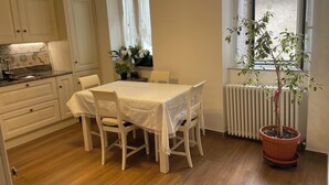 Ein Essbereich mit Tisch für vier Personen, weißen Stühlen, einem Blumentopf und einem Fenster mit Vorhängen.