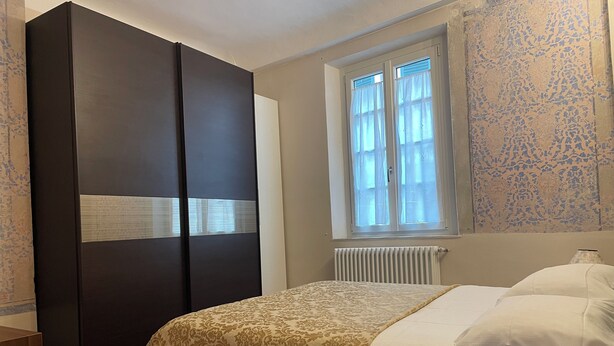 Ein Schlafzimmer mit Bett, Kleiderschrank, einem Fenster mit Vorhängen und einer Heizung.