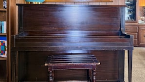 A dark wooden piano with a bench in front, a decorative lamp, and a mirror above the piano.