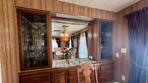 A bedroom with a large wooden dresser, a bed, and a mirror reflecting a dining area.