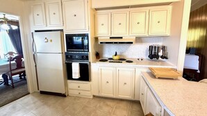 A compact kitchen with white cabinets, a refrigerator, an oven, a stove, and a wooden cutting board.
