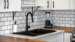 Una cocina con armarios blancos, un grifo negro, una licuadora y un dispensador de jabón.