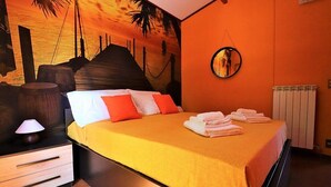 A bedroom with a bed, a nightstand, a lamp, a mirror, and a wall mural. - Villa Lisa: A characteristic and welcoming three-story villa in a quiet position, located on a hillside above the sea, with Free WI-FI. (Sorrento)