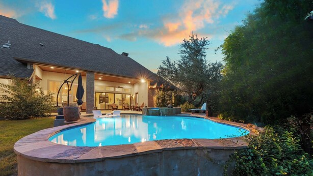 Ein Schwimmbad mit Steinrand, eine überdachte Terrasse und ein Haus mit geneigtem Dach.