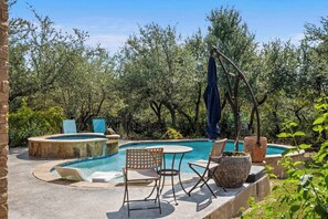 Una piscina con borde de piedra, rodeada de sillas y mesas, y una hamaca colgante.