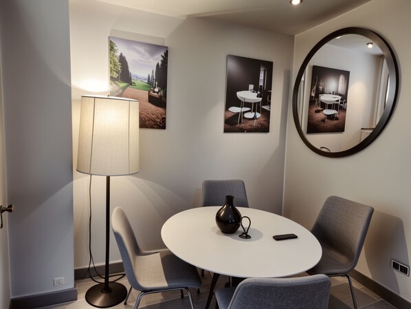 Un comedor moderno con una mesa redonda, sillas grises, una lámpara de pie y dos cuadros en la pared.