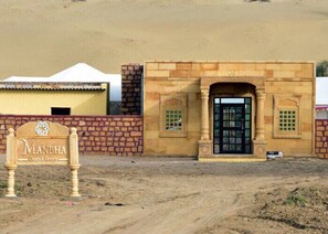 Un edificio con un letrero que dice "MANBHA Camps & Resorts" y una puerta negra con detalles decorativos.