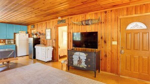 Un intérieur en bois comprenant une cuisine, un coin repas et un salon avec une télévision et une grande porte en bois.