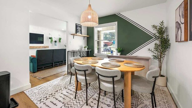 Un espace de salle à manger moderne avec une table en bois, des sets de table en fibres tressées et un luminaire suspendu.