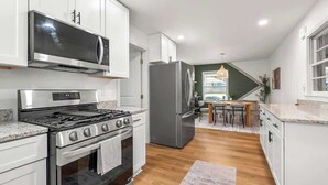 Une cuisine moderne dotée d’appareils électroménagers en acier inoxydable, de meubles blancs et d’un coin repas avec une table et des chaises en bois.