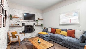 Un salon avec une cheminée, un ensemble de canapés, une table basse et un téléviseur fixé au mur.