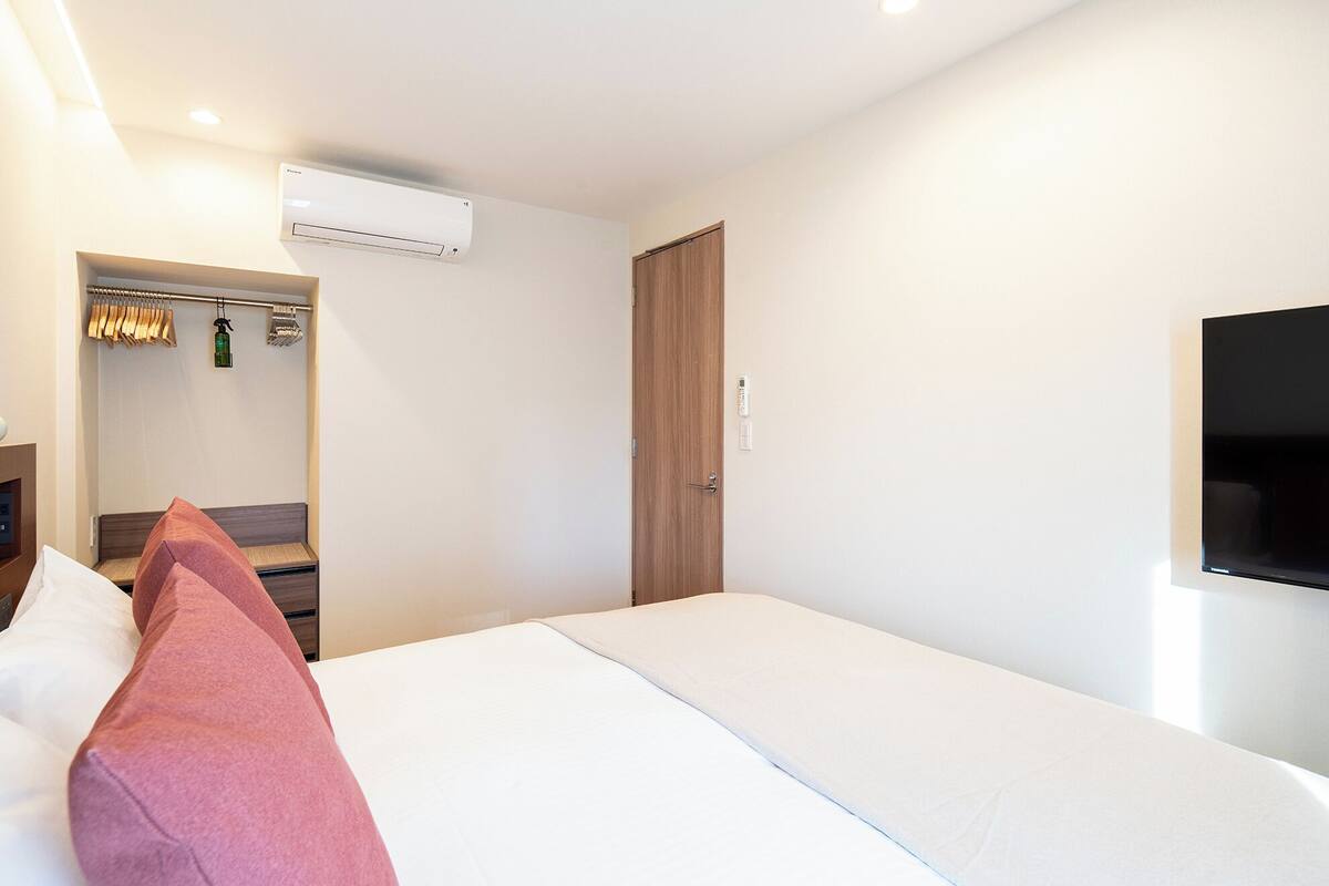 Habitación de hotel con cama, armario, aire acondicionado, televisor y puerta.