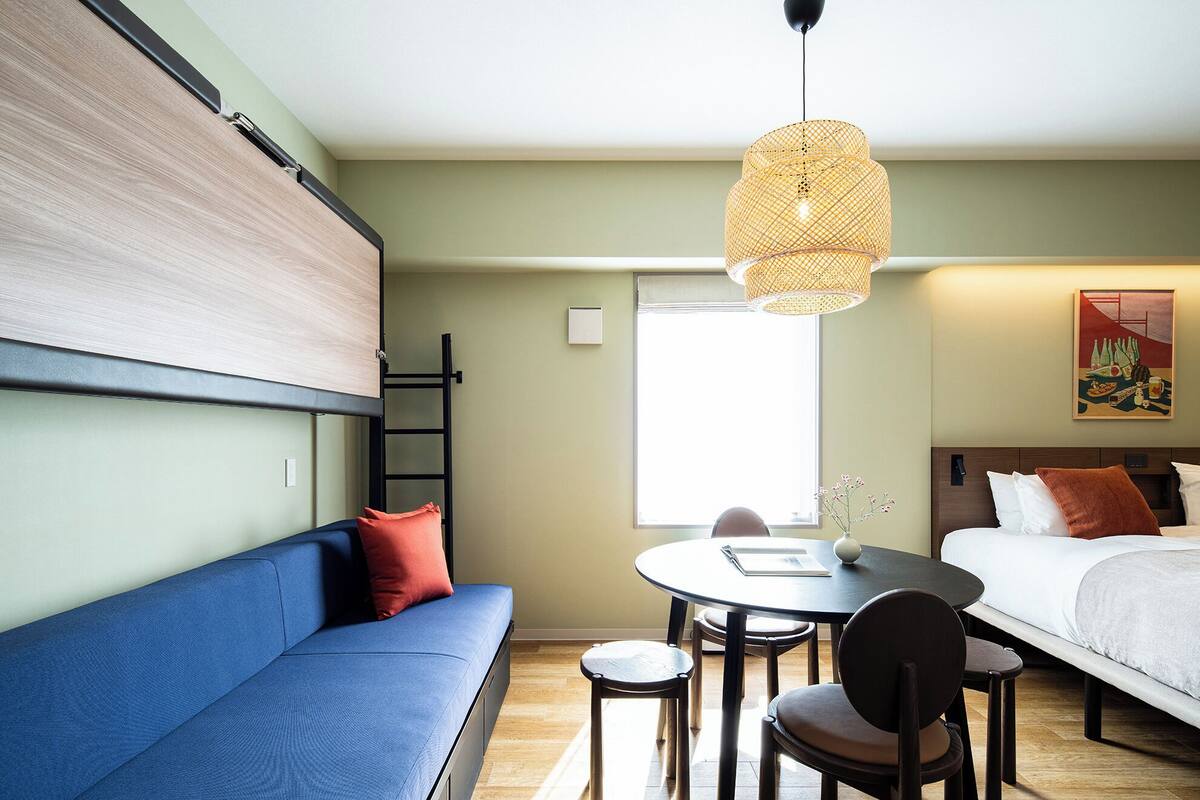 Habitación de hotel compacta con literas, un sofá, una mesa de comedor con sillas y una lámpara colgante.