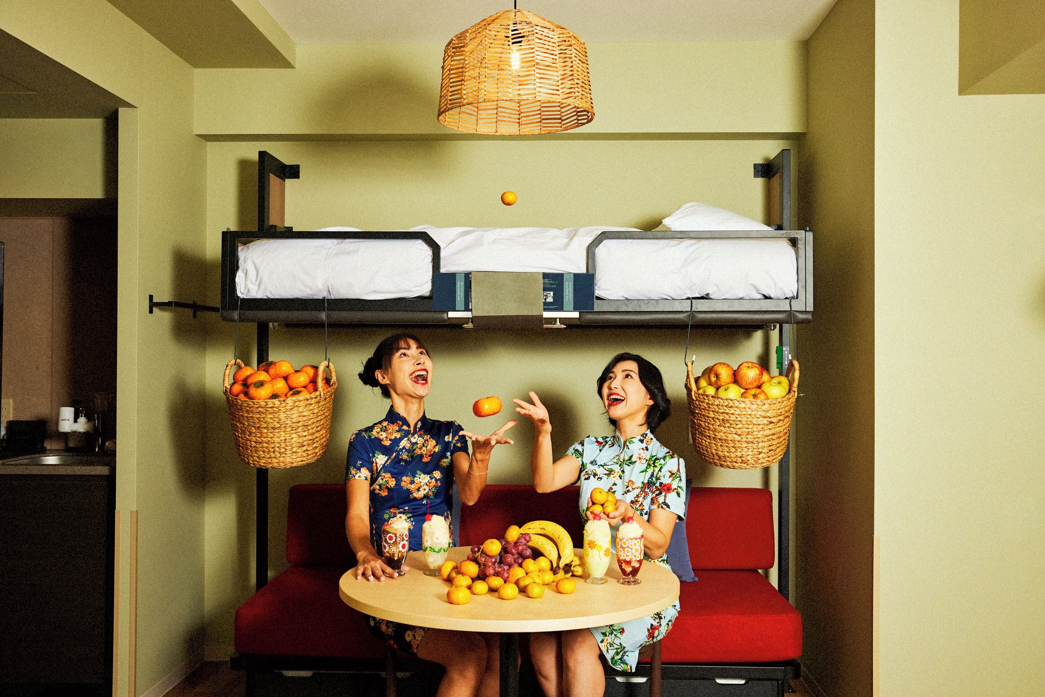 A bunk bed with two beds, a dining table with fruit and drinks, and a hanging basket with oranges.