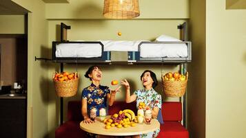A bunk bed with two beds, a dining table with fruit and drinks, and a hanging basket with oranges.
