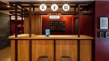 A reception desk with a wooden counter, two stools, a digital screen, and a wall with a grid of small items.