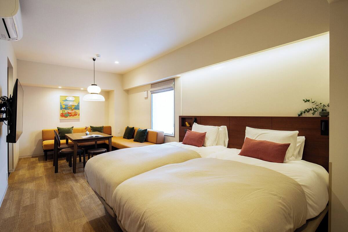 Habitación de hotel con dos camas, un sofá, una mesa de comedor y un televisor.