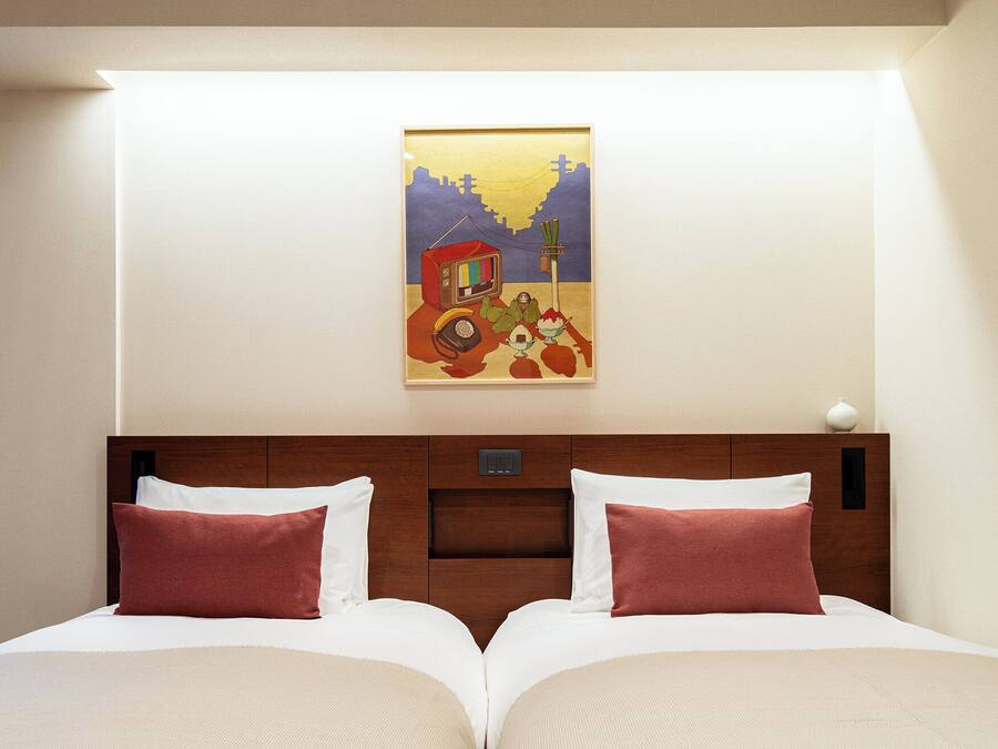 A hotel room with a double bed, two pillows, a wooden headboard, a night switch, and a framed picture on the wall.