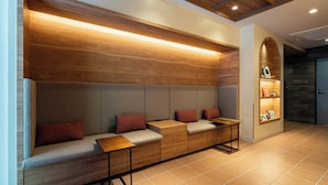 A modern waiting area with a wooden bench, cushioned seating, and a small table. - Section L Ueno-Hirokoji (Tokyo)