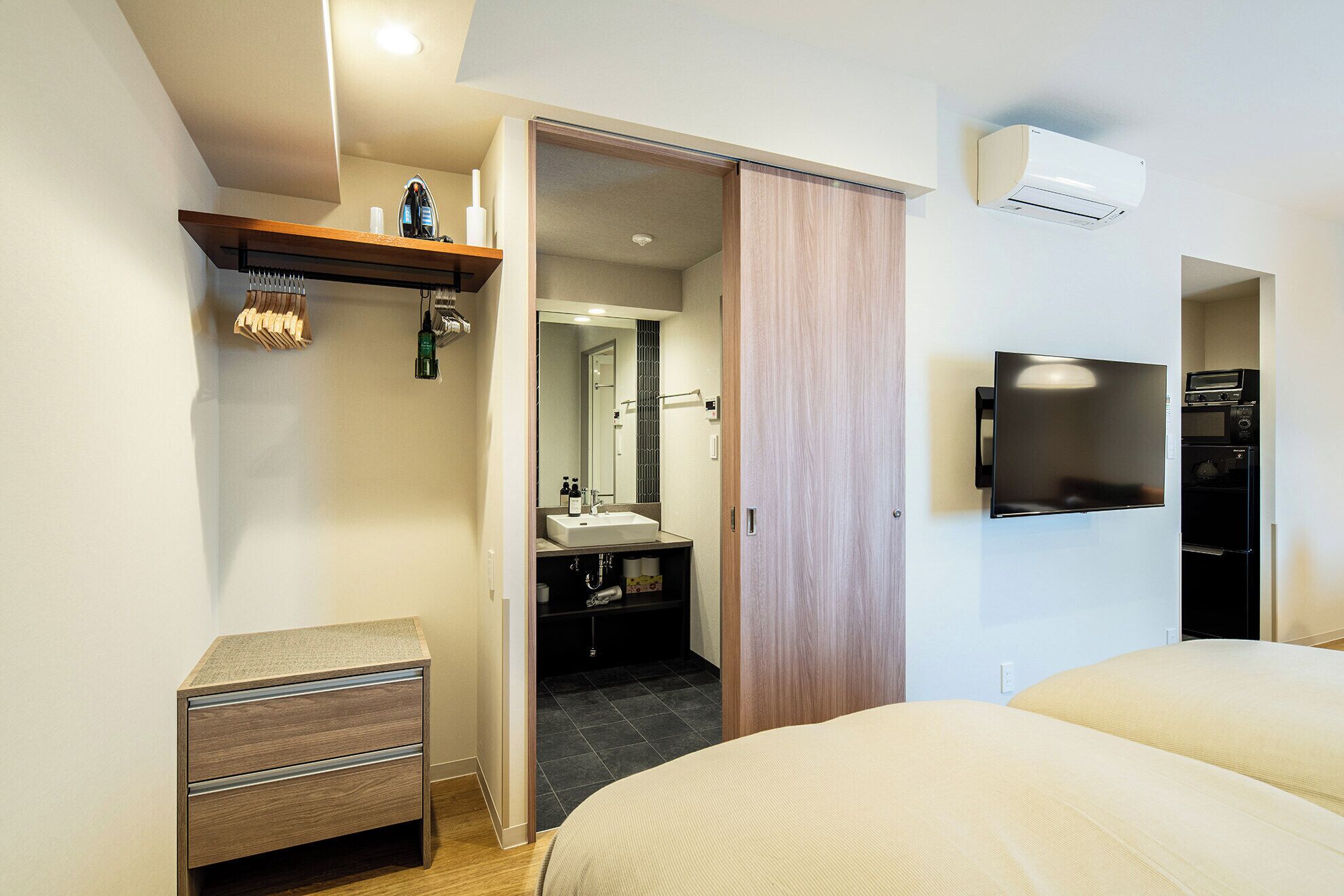 Ein modernes Hotelzimmer mit Bett, Fernseher, flachbildschirm-Fernseher an der Wand, Holzschrank, kleiner Nachttisch und Spiegel.