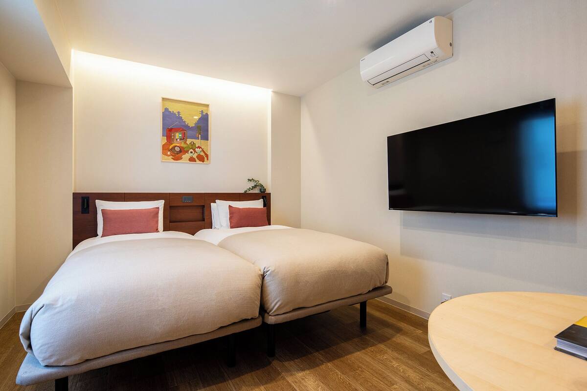 Habitación de hotel con dos camas, un televisor de pantalla plana y una mesita.