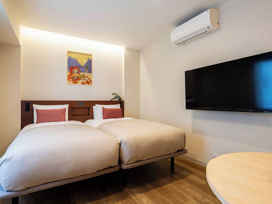 A hotel room with two beds, a flat-screen TV, and a small table.
