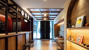 A modern interior with a wooden reception desk, a seating area with a sofa and chairs, and a bookshelf with books and decorative items. - Section L Ueno-Hirokoji (Tokyo)